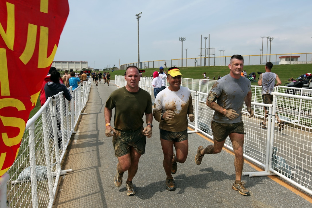 Colonel John E. Merna, commanding officer of the 31st Marine Expeditionary Unit (Left); Sgt. Maj. Gonzalo "Butch" Vasquez, sergeant major of the 31st MEU (center); and Lt. Col. G. T. Roesti, executive officer of the 31st MEU (right), cross the finish line of the 10K mud run here, March 30. Hundreds of competitors from all over the island gathered to participate in the run, which was put together by Marine Corps Community Services and the Single Marine Program. The run included obstacles that required runners to wade through shin-deep water, scale a five foot wall, and traverse thick patches of mud.