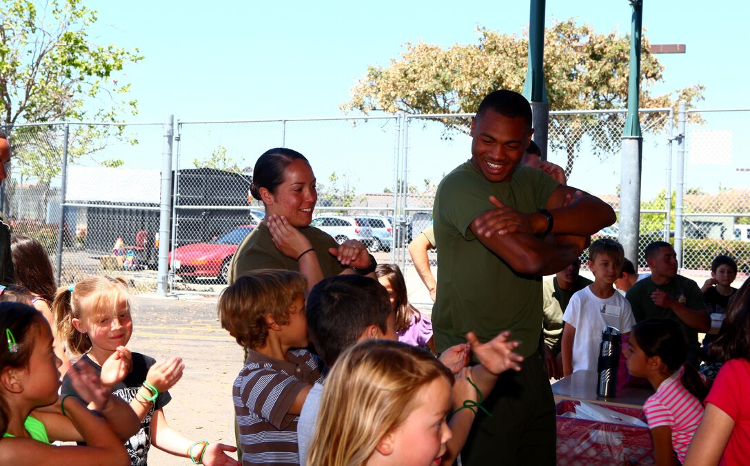 Cpl. Andre Fradiue, right, a Palmdale, Calif., native, and Pfc. Madison Hopkins, left, an Orange, Calif., native, both volunteers from Marine Tactical Air Command Squadron 38, teach students how to dance the Macarena at lunch during a Single Marine Program fitness challenge at Kumeyaay Elementary School in San Diego, April 19. During lunch and at recess, Marines interacted and played with the children and answered questions about their daily lives.