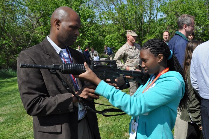 Shawn Taylor of Resource Management helps his daughter Micah with a weapon at the Infantry Combat Equipment display April 25 during Marine Corps Systems Command's "Bring Your Daughters and Sons to Work Day." 