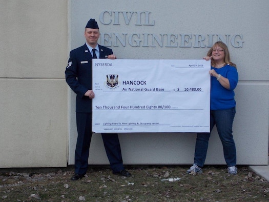 New York Air National Guard Staff Sgt. Joshua Fuqua (left), Engineering Assistanst with the 174th Attack Wing's Civil Engineering Squadron, and Mrs. Danita Kinner, Civil Engineering Resource Advisor, pose with a $10,480 rebate check received from NYSERDA outside the civil engineering building at Hancock Field Air National Guard Base, Syracuse, NY. The check was a result of energy conservation at Hancock Field due to installation of new lighting and occupancy sensors. (Photo by Mr. John Muller/Released)