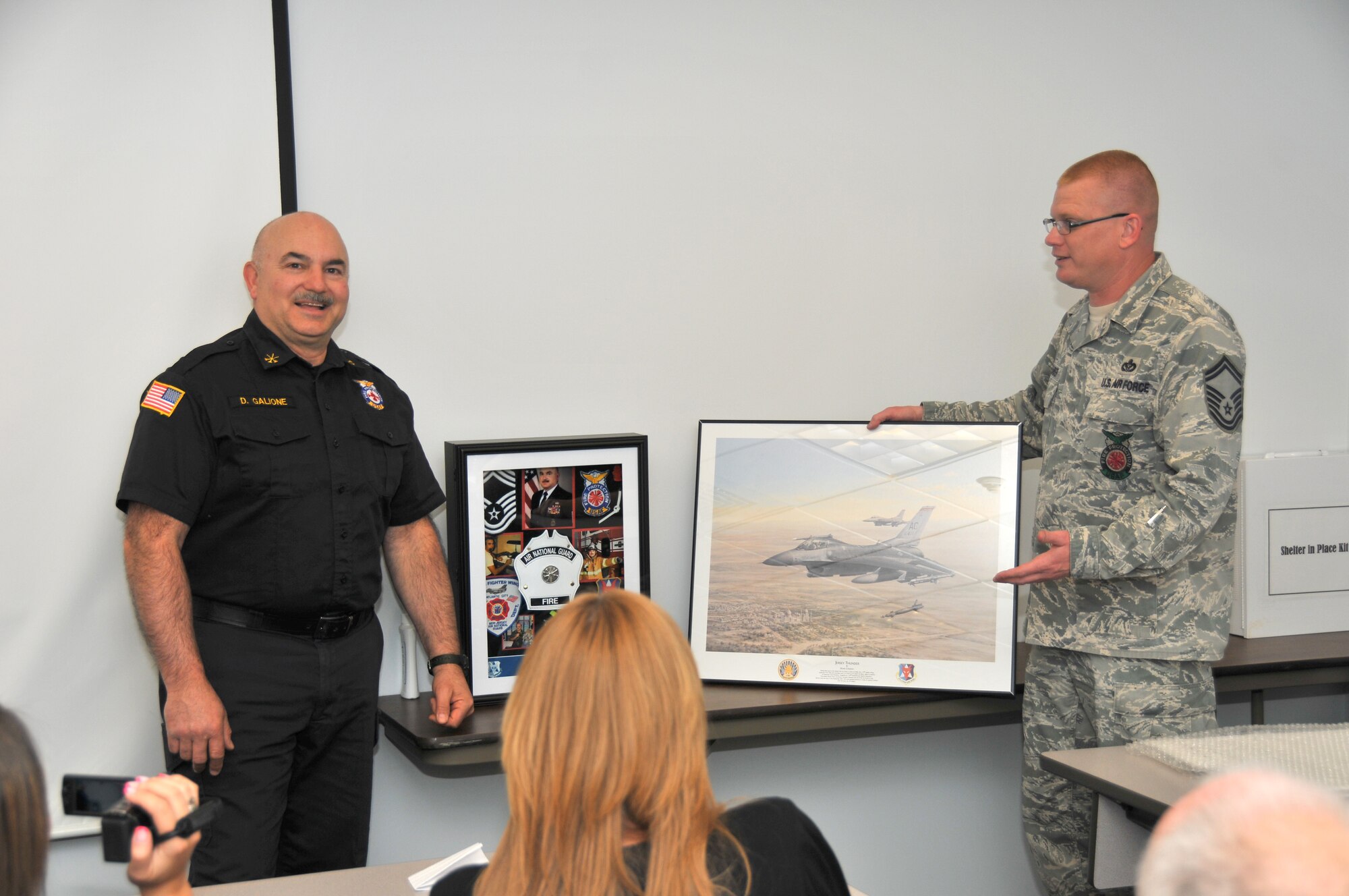 A picture of Chief Master Sgt. Dominick Galione (Ret.) accepting a lithograph from Senior Master Sgt. Brian Alexander upon his retirement.