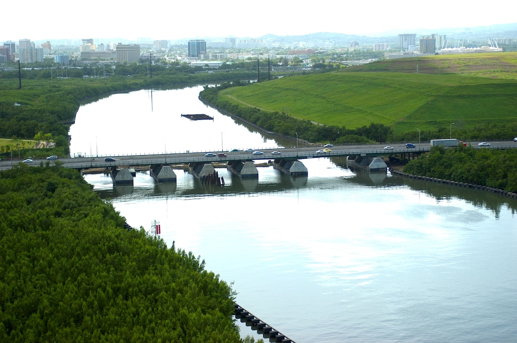 Looking upstream to its source in the central mountains, the Río Puerto Nuevo basin drains 24 square miles of metropolitan San Juan, 75 percent of which is highly developed with a population of 250,000. The plan of improvements includes channels, high velocity channels, debris basins and modifications to bridges, in an effort to protect the population against a 100-year flood. 