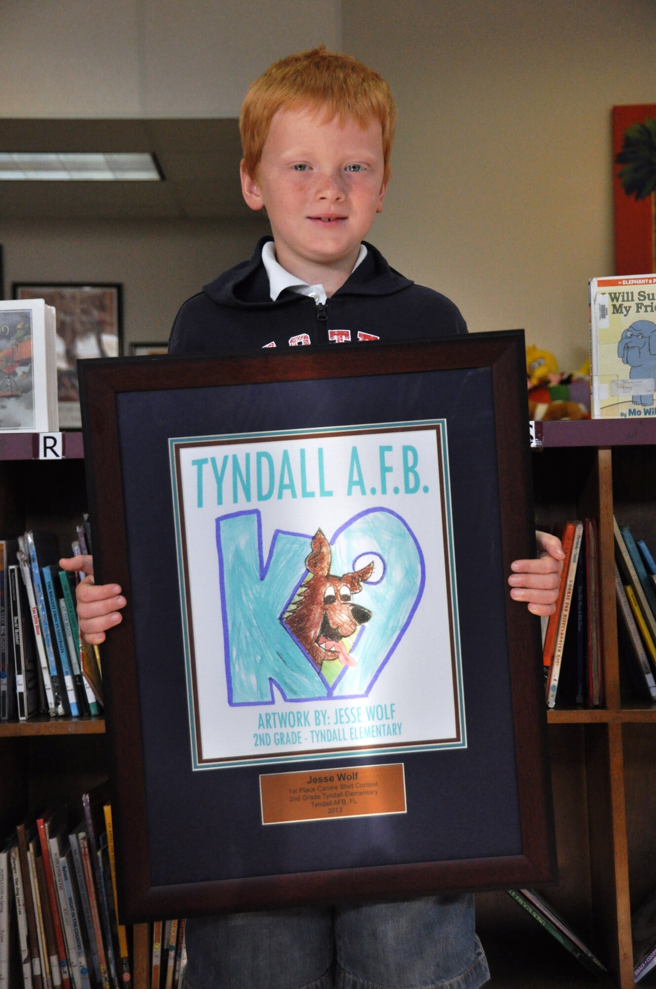Tyndall Elementary School second-grader Jesse Wolf poses with the military working dog T-shirt contest award April 26 at Tyndall Elementary School. Jesse designed the winning T-shirt that will be given away at the 325th SFS Kennel during their demos. (U.S. Air Force photo by Airman 1st Class Alex Echols) 