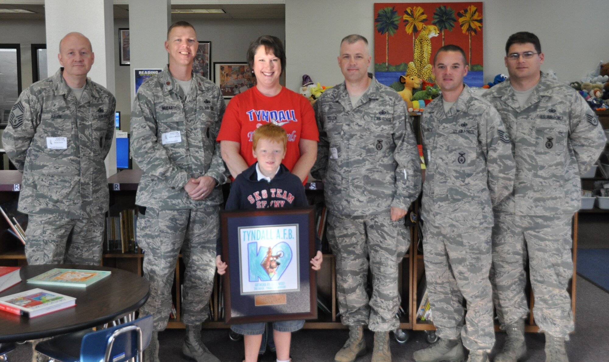 Members of the 325th Security Forces Squadron, Mrs. Susan Ross, Tyndall Elementary School principal, and Tyndall Elementary School second-grader Jesse Wolf  pose with the military working dog T-shirt contest award April 26 at Tyndall Elementary School. Jesse designed the winning T-shirt that will be given away at the 325th SFS Kennel during their demos. (U.S. Air Force photo by Airman 1st Class Alex Echols)