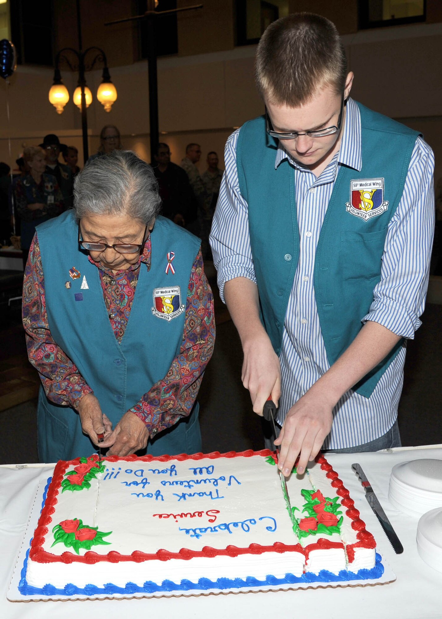 Trinidad Garcia and Nate Olech, volunteers at the Wilford Hall Ambulatory Surgical Center, serve cake at the atrium during the National Volunteer Week celebration April 24, 2013, at Joint Base San Antonio-Lackland, Texas.  A volunteer for more than 30 years, Garcia turns 93 years at the end of May, making her the oldest volunteer at WHASC. Olech is currently 17 years old, making him the youngest volunteer at WHASC. Established in 1974, National Volunteer Week recognizes the impact of volunteerism on America. The week-long event draws the support and endorsement of the president, Congress, governors, mayors and municipal leaders, as well as corporate and community groups across the nation. (U.S. Air Force photo/Harold China)