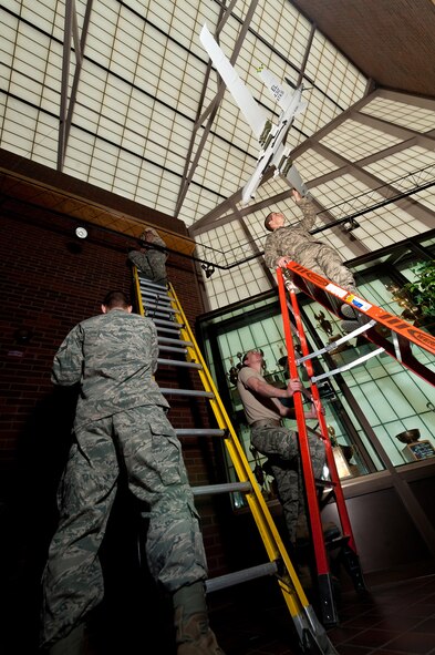 Airmen from the 28th Civil Engineer Squadron Structures Flight hang a scale model of an MQ-9 Reaper in the 28th Bomb Wing Headquarters lobby at Ellsworth Air Force Base, S.D., May 1, 2013. The MQ-9 model is the newest addition to the lobby, which also features scale models of a B-1 and B-17, aircraft that either currently or historically operated from the base. (U.S. Air Force photo by Tech. Sgt. Nathan Gallahan/Released)