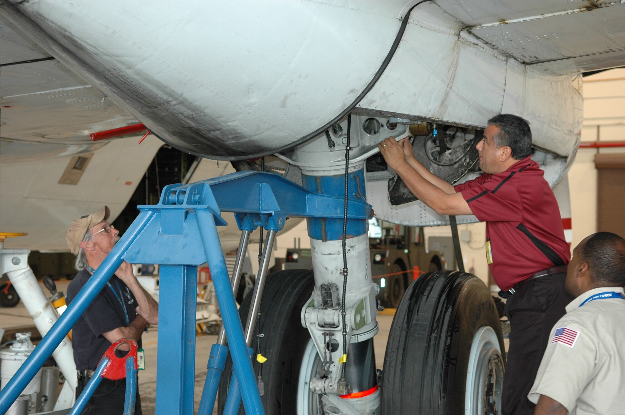 Frank Montes, DynCorp International maintenance supervisor who looks over the Super Guppy, tinkers with the main landing gear during an April 25 inspection as Todd Flannery, left, DynCorp quality assurance representative, and Nelson Reyes, DynCorp flight engineer, look on. (Air Force photo by Brandice J. O’Brien)