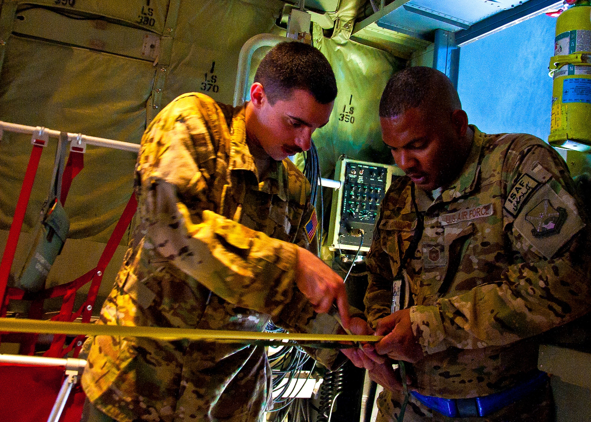 (Right) Master Sgt. DeMond Connors holds the measuring tape while Airman 1st Class Justin McKenzie cuts a length of 550 cord to tie together bundles on a C-130J Hercules April 29. Both Airmen are with the 772nd Expeditionary Airlift Squadron and were securing the bundles as part of Extracted Container Delivery System, a new, more accurate, method of airdrop designed to pull the bundles out of the aircraft faster. Connors and McKenzie are both deployed from Little Rock Air Force Base, Ark. (U.S. Air Force photo by Senior Airman Scott Saldukas)