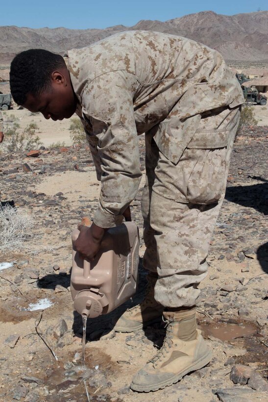 Sergeant Jevin U. Rainey, a field radio operator serving with Headquarters Battalion, 1st Marine Division, pours water to dissolve salt during Exercise Desert Scimitar here, May 2, 2013. Rainey, a 27-year-old native of Schenectady, N.Y., added salt to the soil to increase its conductivity, strengthening the grounding for nearby antennas. Proper grounding increases the range and clarity of radio transmissions. (U.S. Marine Corps photo by Sgt. Jacob H. Harrer)