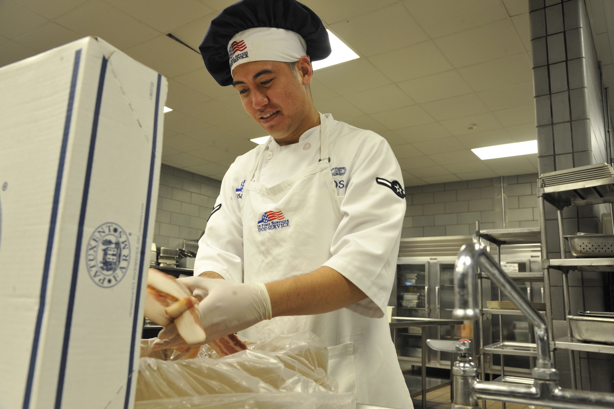 Airman Eric Sadsad, 509th Support Squadron services apprentice, removes bacon from a box at the Ozark Inn on Whiteman Air Force Base, Mo. April 15, 2013. Sadsad and other food services staff members prepare food to keep incoming shift workers on schedule (U.S. Air Force photo by Airman 1st Class Keenan Berry/Released)
