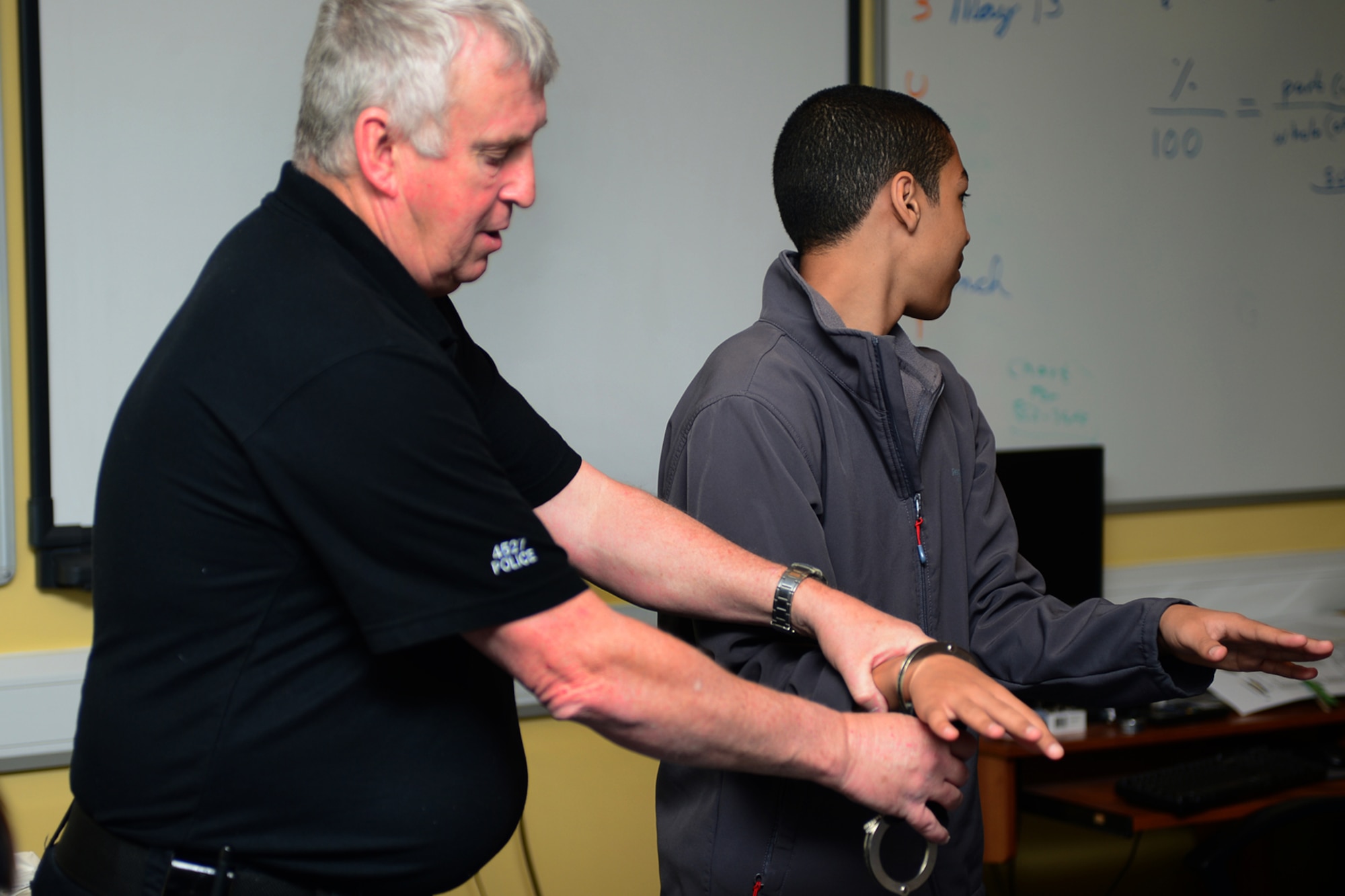 ROYAL AIR FORCE FELTWELL, England -- Police Constable Paul Glover, Ministry of Defence Police, demonstrates arresting procedures on eighth-grader Elijah Miller, son of Master Sgt. Ron Miller, 48th Munitions Squadron munitions inspection section chief, during the Lakenheath Middle School U.K. Day May 3, 2013.  U.K. Day is an annual event designed to educate children on U.K. customs, history and heritage and to foster a relationship with the host nation. (U.S. Air Force photo by Airman 1st Class Dana J. Butler)