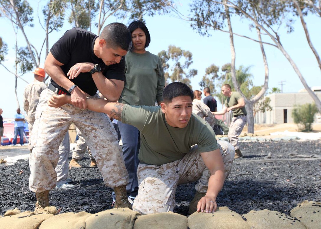 Staff Sgt. Gilberto Castillo, a Marine Corps martial arts instructor trainer and Lance Cpl. Jon Nguyen, a field wireman, with 9th Communication Battalion, demonstrates an arm bar takedown for Christina Pintos, spouse of Sgt. Alex Pintos, with 9th Comm. Bn., during a Jane Wayne Day at Camp Pendleton, Calif., May 4. Jane Wayne Day is an opportunity for Marine spouses to 'walk a mile' in the shoes of their Marines. The 9th Comm. Bn., spouses viewed equipment their Marines use day-to-day and were afforded the chance to experience some of the training they go through.
