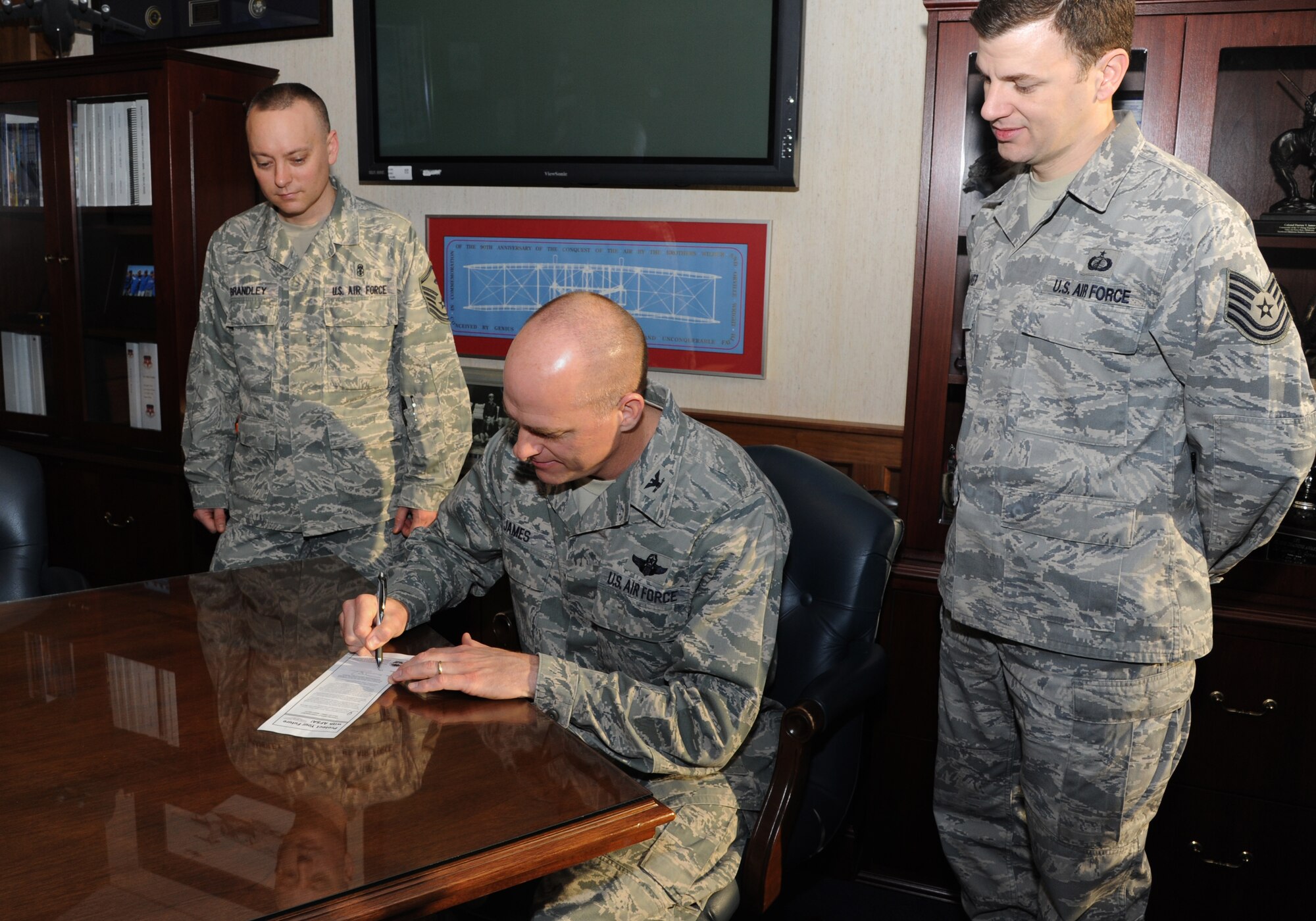 Master Sgt. Phillip Brandly, the 71st Mission Support Group first sergeant, left, and Tech. Sgt David Weaver, right, the NCO in charge customer service in the 71st Comptroller Squadron, watch as Col. Darren James, center, the 71st Flying Training Wing commander, signs his membership the Air Force Sergeants Association at Vance Air Force Base, Okla April 25. James became one the first Air Force officers to join the Chapter 990.