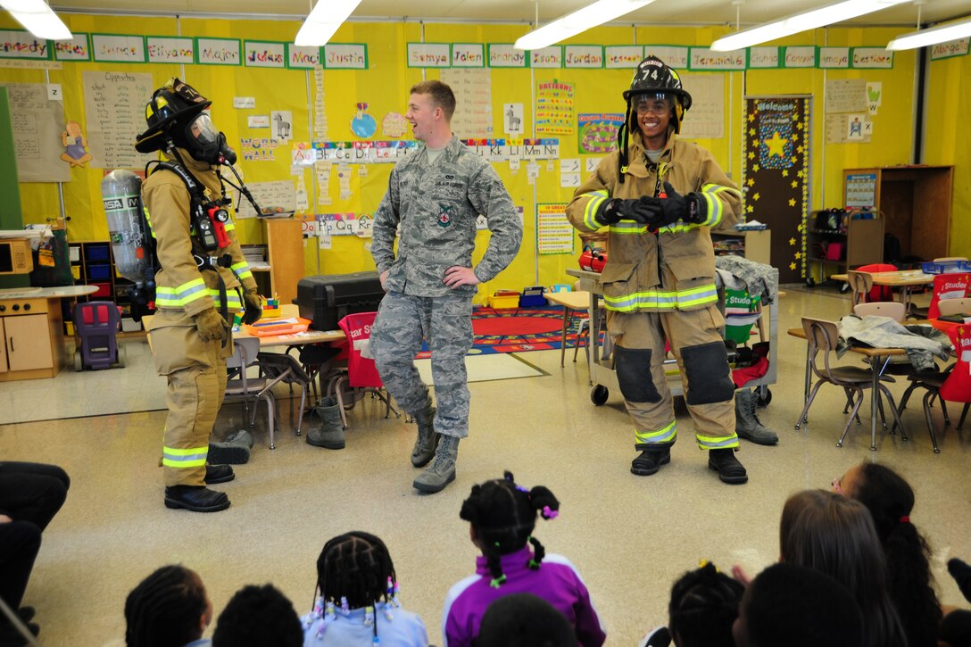 11th Civil Engineer Squadron firefighters, Airmen 1st Class Scott Burdick and Tevin Charles race to don their gear in record time as Airman Jared Becker times them to show local elementary kindergartners fire safety skills, May 3, 2013, at a career day event. The children applauded their efforts afterward. (U.S. Air Force photo/Staff Sgt. Amber Russell)