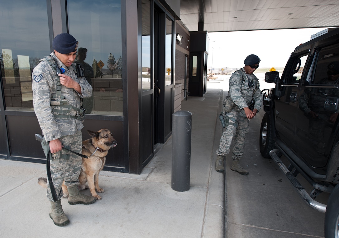 Staff Sgt. Michael Gwin, 28th Security Forces Squadron military working dog handler, his dog Rex, and Airman Keith Leflore, 28th SFS defender, stand ready at the gate at Ellsworth Air Force Base, S.D., April 25, 2013. Defenders guard the Liberty Gate 24 hours a day by defenders to keep the base secure. (U.S. Air Force photo by Airman 1st Class Alystria Maurer/Released)  