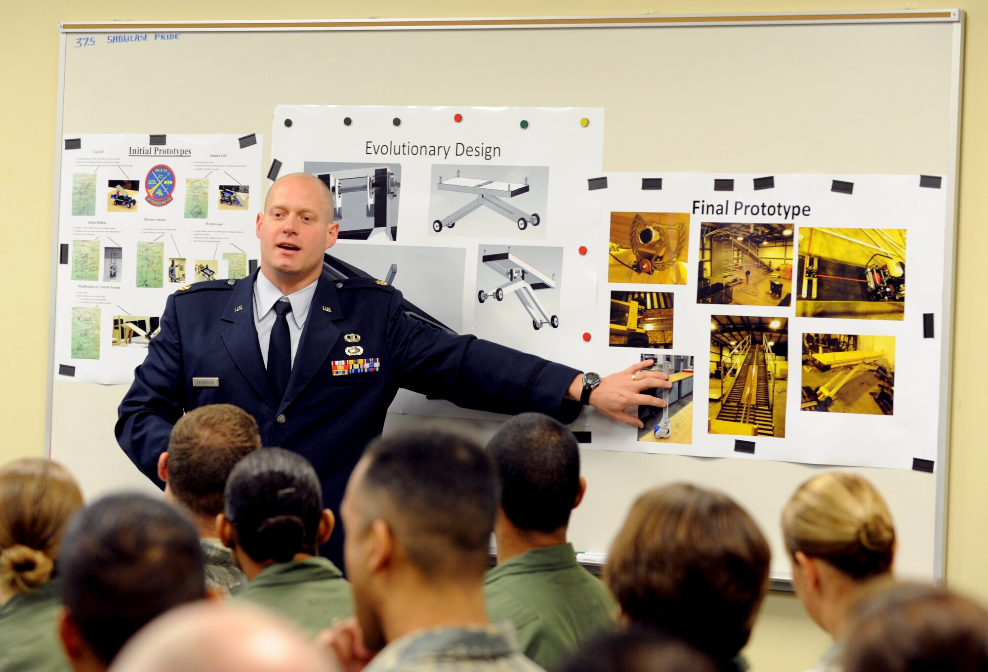 Maj. Cody Rasmussen, U.S. Air Force Academy engineering mechanics department advisor, shows 375th Aeromedical Evacuation Squadron members photos of the final patient loading system prototype during the Capstone project presentation.  Seven senior cadets worked on enhancing features to the current PLS.