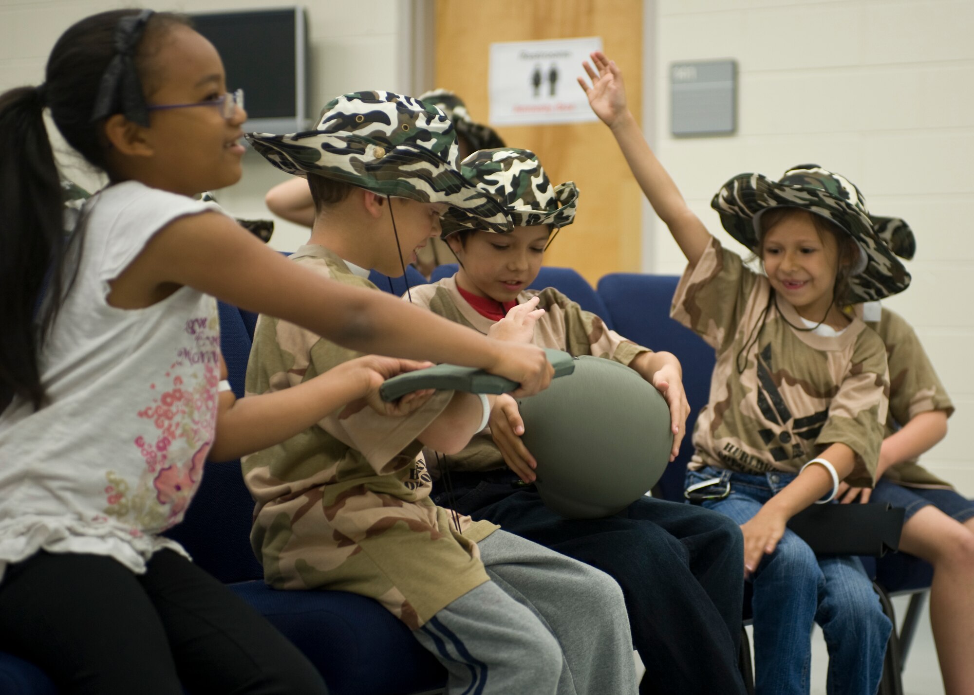 Children pass around a rifle plate and helmet during the Kids Understand Deployment Operations event at the Deployment Control Center auditorium on Hurlburt Field, Fla., April 27, 2013.  This part of the event showcased various tactical gear that Airmen must acquire and eventually wear, before deploying.   (U.S. Air Force photo by Airman 1st Class Hayden K. Hyatt)