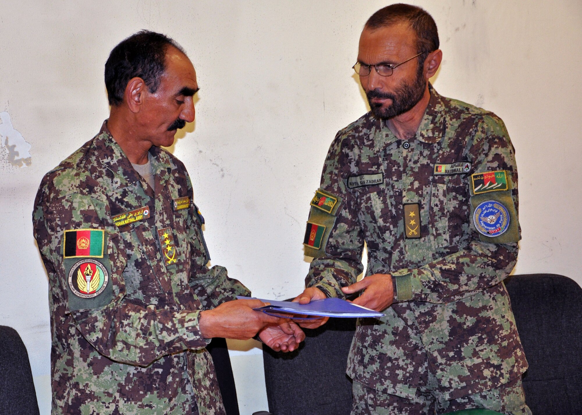 Afghan Air Force Lt. Col. Raees Khan, PeH education planning officer, official hands over six newly signed training decrees to Col. Mahmood Rahman, Commandant of Pohantoon-e-Hawayee “Air University”, in a ceremony May 4, 2013 at Kabul International Airport, Afghanistan. The development of the decrees was a team effort between the PeH leadership and their advisors from NATO Air Training Command-Afghanistan. The implementation of these decrees marks the first time in the school’s history to have standard operating procedures for the teaching of the students. (U.S. Air Force photo/Capt. Anastasia Wasem)