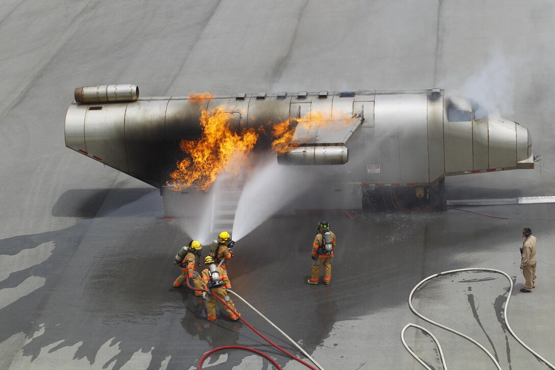 Firefighters battle a fire during a mobile aircraft fire training device exercise at the Camp Hansen Joint Training Facility May 2. Firefighters used the device to create controlled burns in a replicated fuselage. The flames, coupled with smoke machines and audio devices, create realistic training conditions for the firefighters. The firefighters are with Marine Corps Installation Pacific Fire and Emergency Services. Photo by Lance Cpl. Henry J. Antenor