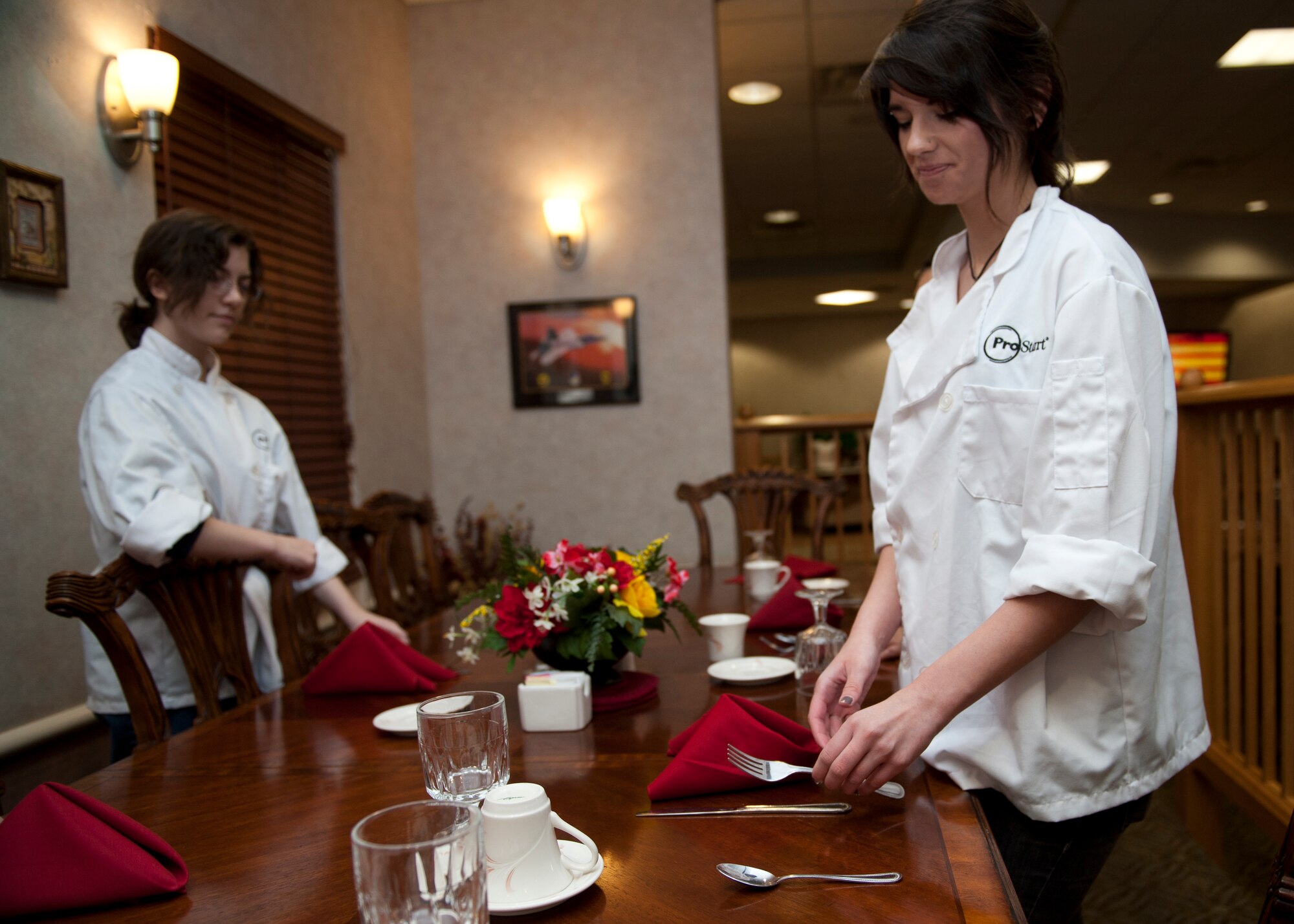 Two culinary students from various local high schools learn napkin- folding and table set-up at the Shifting Sands Dining Facility on Holloman Air Force Base, N.M., May 8. The students visited the Shifting Sands Dining Facility to learn how the military plans, prepares and serves thousands of meals a day to its personnel. The students were divided into small groups and received hands-on experience in napkin folding, garnishing, serving and cooking. (U.S. Air Force photo by Airman 1st Class Colin Cates/Released)