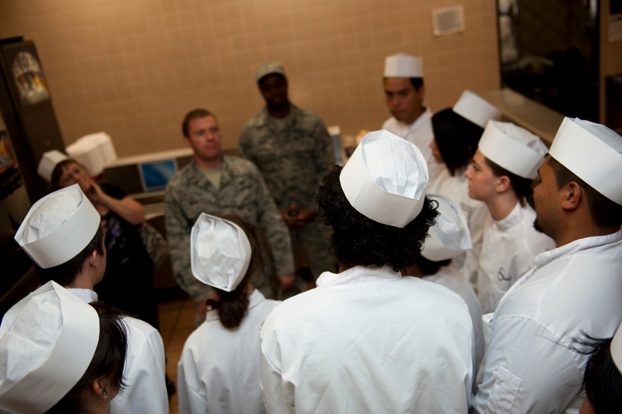 Culinary students from various local high schools receive a briefing about everyday operations at the Shifting Sands Dining Facility by their staff at Holloman Air Force Base, N.M., May 8. The students visited the Shifting Sands Dining Facility to learn how the military plans, prepares and serves thousands of meals a day to its personnel. The students were divided into small groups and received hands-on experience in napkin folding, garnishing, serving and cooking. (U.S. Air Force photo by Airman 1st Class Colin Cates/Released) 