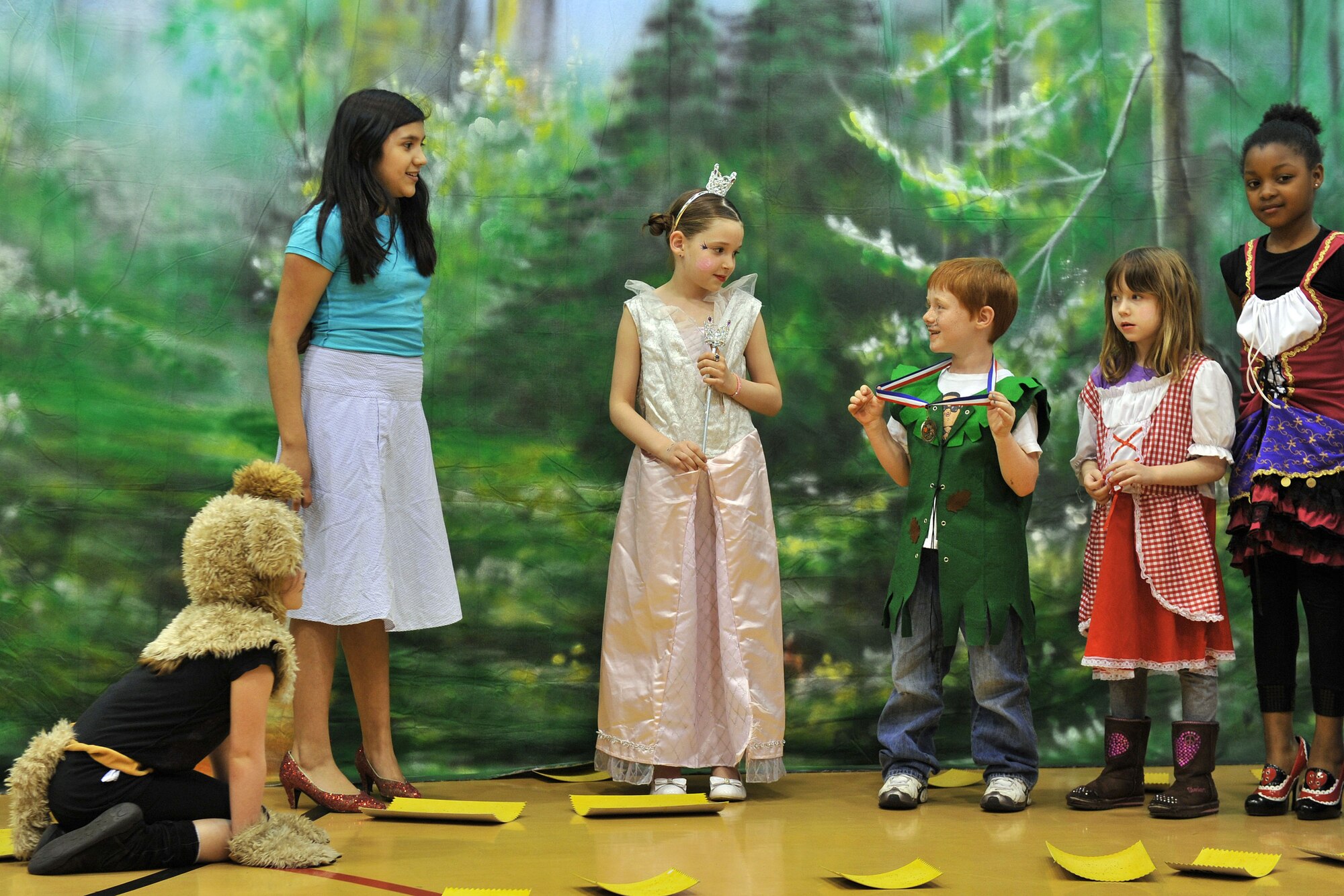 From left, Toto the Dog, played by Paige Lacey; Dorothy, played by Gloryssel Moreno; the Good Witch, played by Calla Fisher; the Mayor of Munchkinland, played by Adam Hardin; and resident munchkins, played by Kaitlyn Walton and Aalahnta Anthony, converge after Dorothy's house drops on the Wicked Witch of the East during the production of the “Wizard of Oz” May 7, 2013, at the youth center on RAF Mildenhall, England. After the house dropped on the Wicked Witch of the East, the Good Witch instructed Dorothy to put on the ruby slippers, as they have magical powers. Twenty-four children participated in the play, bringing the imaginative work of L. Frank Baum to life. (U.S. Air Force photo by Tech. Sgt. Stacia Zachary/Released)