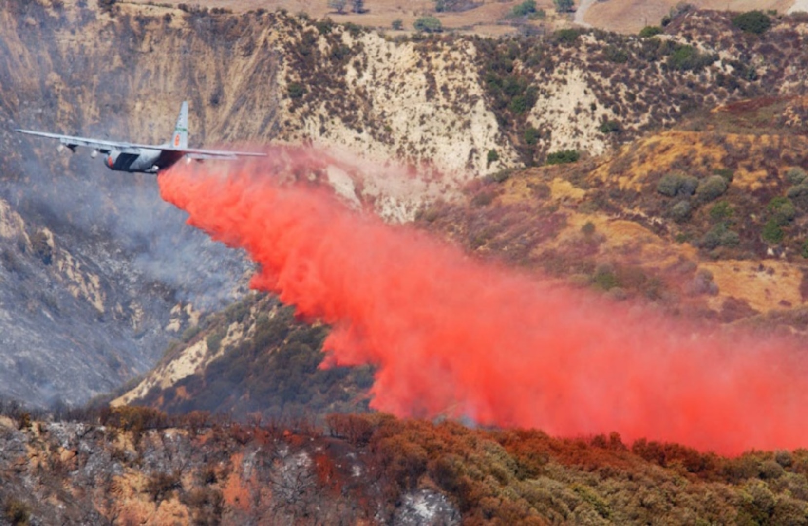 A MAFFS (Modular Airborne Fire Fighting System) equipped C-130E aircraft from the 146th Airlift Wing, Channel Islands Air National Guard Station, makes a Phoschek fire retardant drop on the Simi Fire in Southern California.