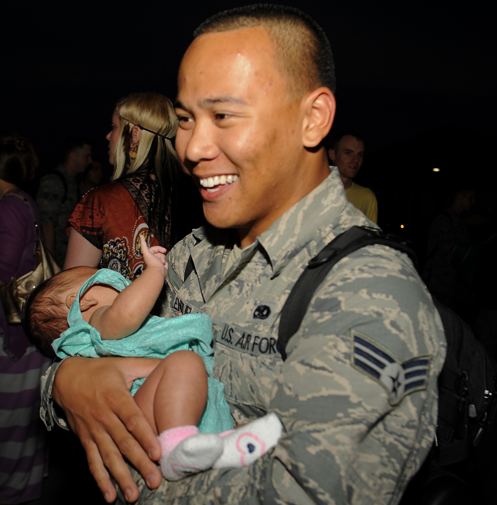 U.S. Air Force Senior Airman Nico Valeazuela, 18th Munitions Squadron munitions systems crew chief, holds his daughter for the first time on Kadena Air Base, Japan, May 9, 2013, after returning from a deployment. More than 60 Airmen returned from the eight-month deployment and spouses made various baked goods and banners for their arrival. (U.S. Air Force photo by Airman 1st Class Malia Jenkins/Released)