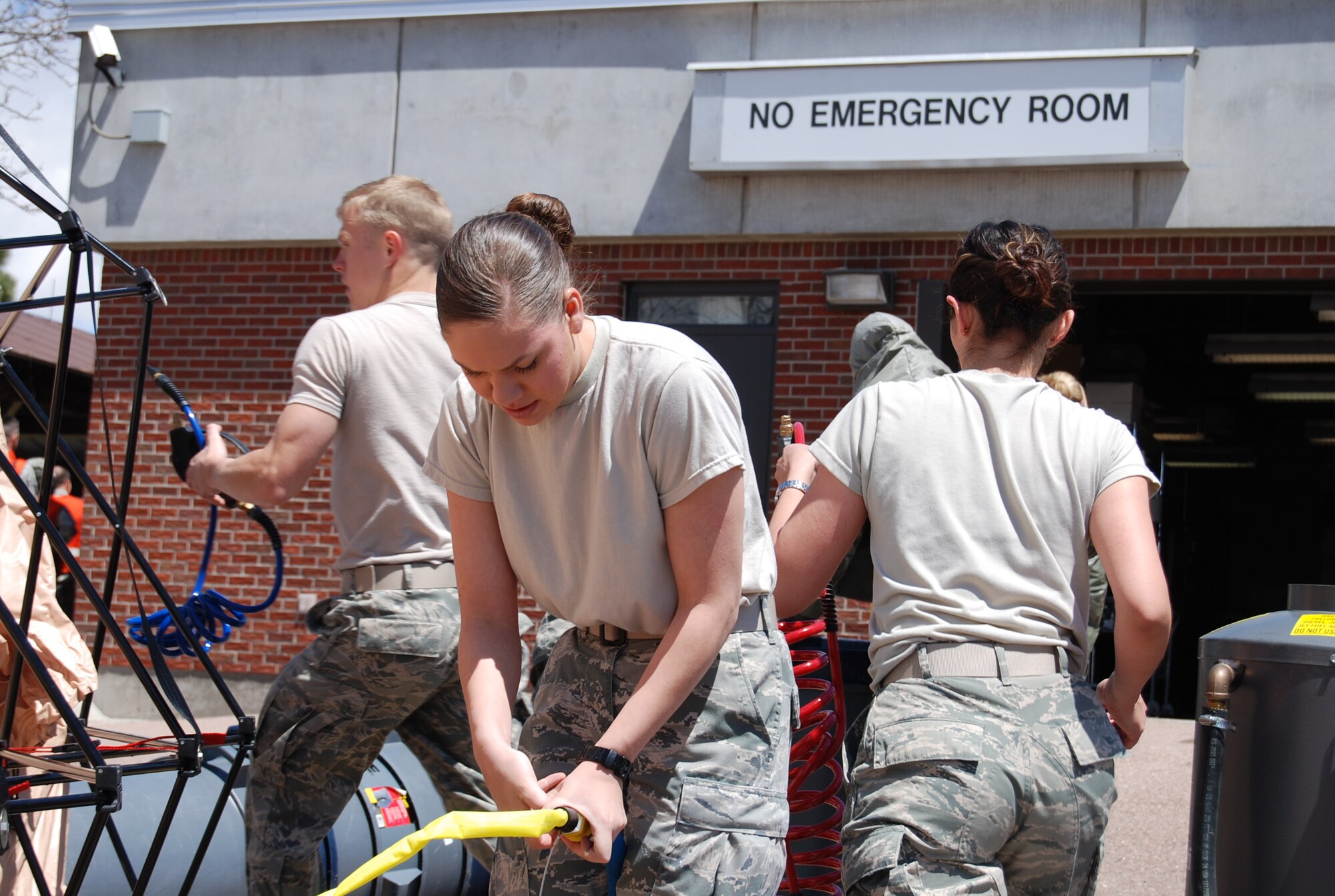 Airmen work together to expedite the setup of a decontamination tent outside of the 21st Medical Group building while additional personnel work to calm and assess the exposed patients. The decontamination tent is the first line of defense when neutralizing the chemical agent allowing the patient to receive further treatment. (U.S. Air Force photo/Michael Golembesky)
