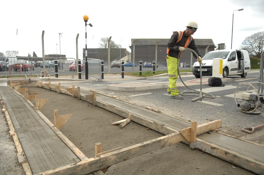 A contractor cleans up the area after concrete is laid in preparation of installation of a new vehicle access control barrier April 18, 2013, on Lincoln Road, RAF Mildenhall, England. Fifteen new barriers are currently being installed around the base to increase force protection and will save the base both time and money, as well as being environmentally-friendly. (U.S. Air Force photo by Airman 1st Class Dillon Johnston/Released)