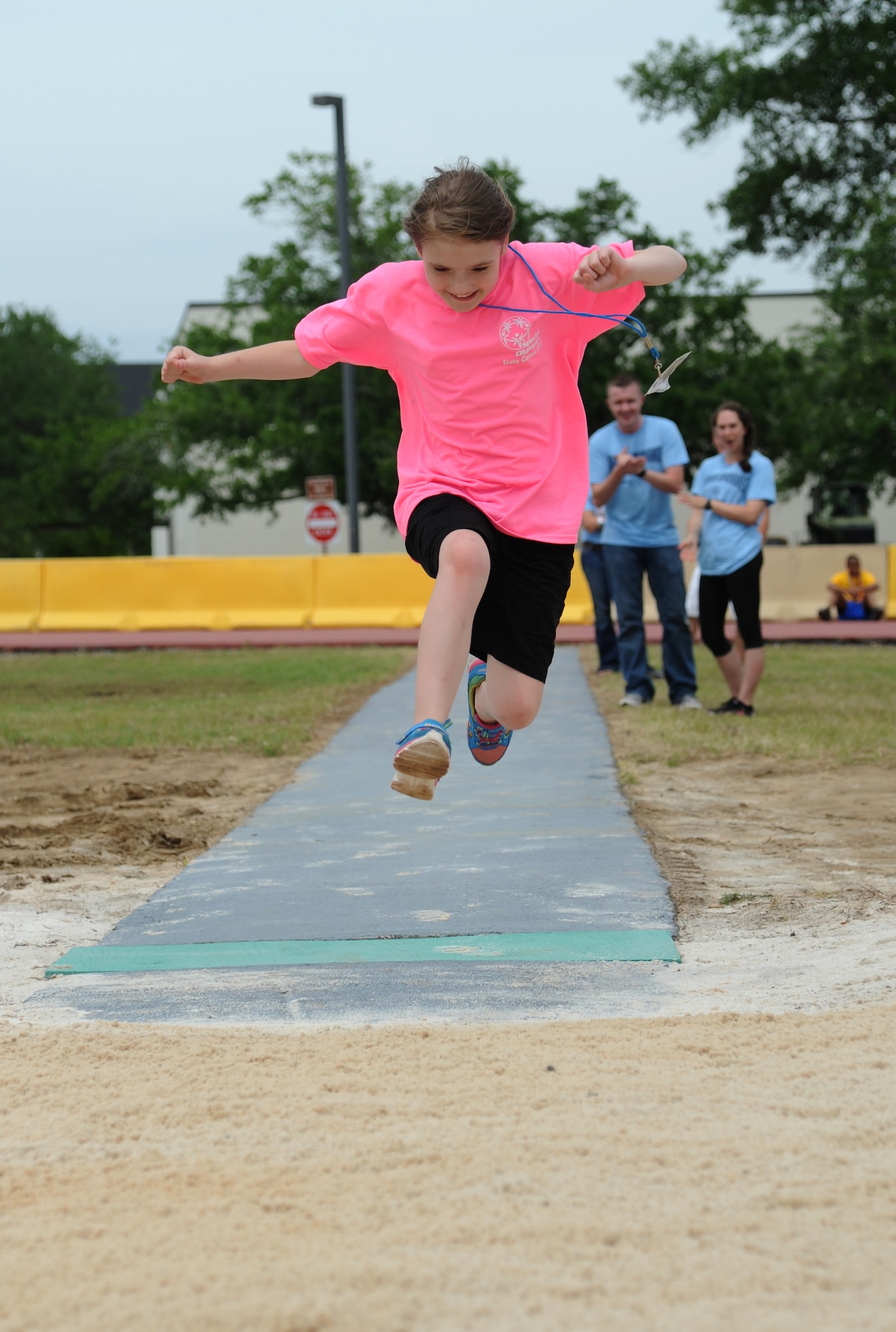 Reana, athlete, leaps into the air during the running long jump competition as her sponsors Airman Basic Timothy Weir, 338th Training Squadron, and Airman Jennifer Soucy, 334th TRS, cheer her on at the Special Olympics Mississippi Summer Games on May 11, 2013, at Keesler Air Force Base, Miss.  More than 900 athletes and 3,000 volunteers worked together to hold competitions throughout the day.  This is the 27th year Keesler has hosted the state Special Olympics.   (U.S. Air Force photo by Kemberly Groue)