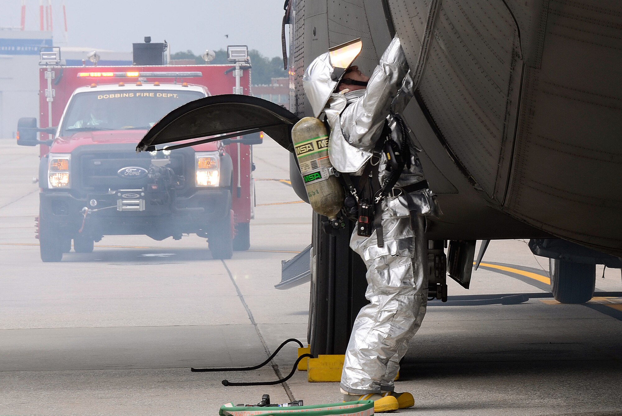 A member of the Dobbins Fire Department raises the troop door searching for injured crew members as emergency response teams respond to a simulated scenario involving a collision of an aircraft refueling truck and a C-130 Hercules during a major accident response exercise (MARE) held on Dobbins Air Reserve Base, Ga. May 10. (U.S. Air Force photo/Don Peek)