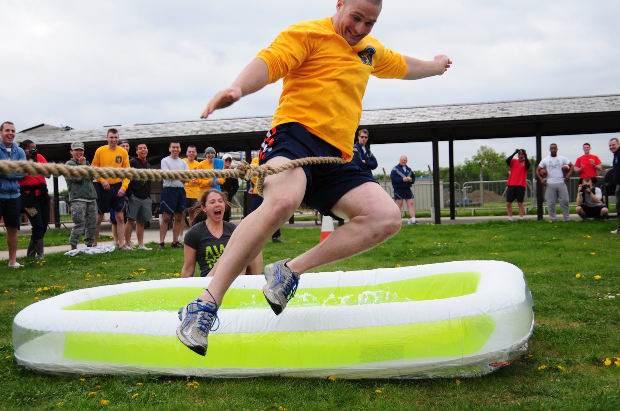 Airman 1st Class Thomas Devereaux, 100th Operations Support Squadron Aircrew Flight Equipment apprentice , takes a flying leap over a small, inflatable pool – narrowly avoiding a soaking – as his team is pulled over the line by 100th Maintenance Squadron members during the tug-of-war event May 10, 2013, at a post Unit Effectiveness Inspection celebrations on RAF Mildenhall, England. Airmen eating barbecue and taking part in sporting events including arm wrestling, kick ball and “slip-n-slide.” (U.S. Air Force photo by Karen Abeyasekere/Released)