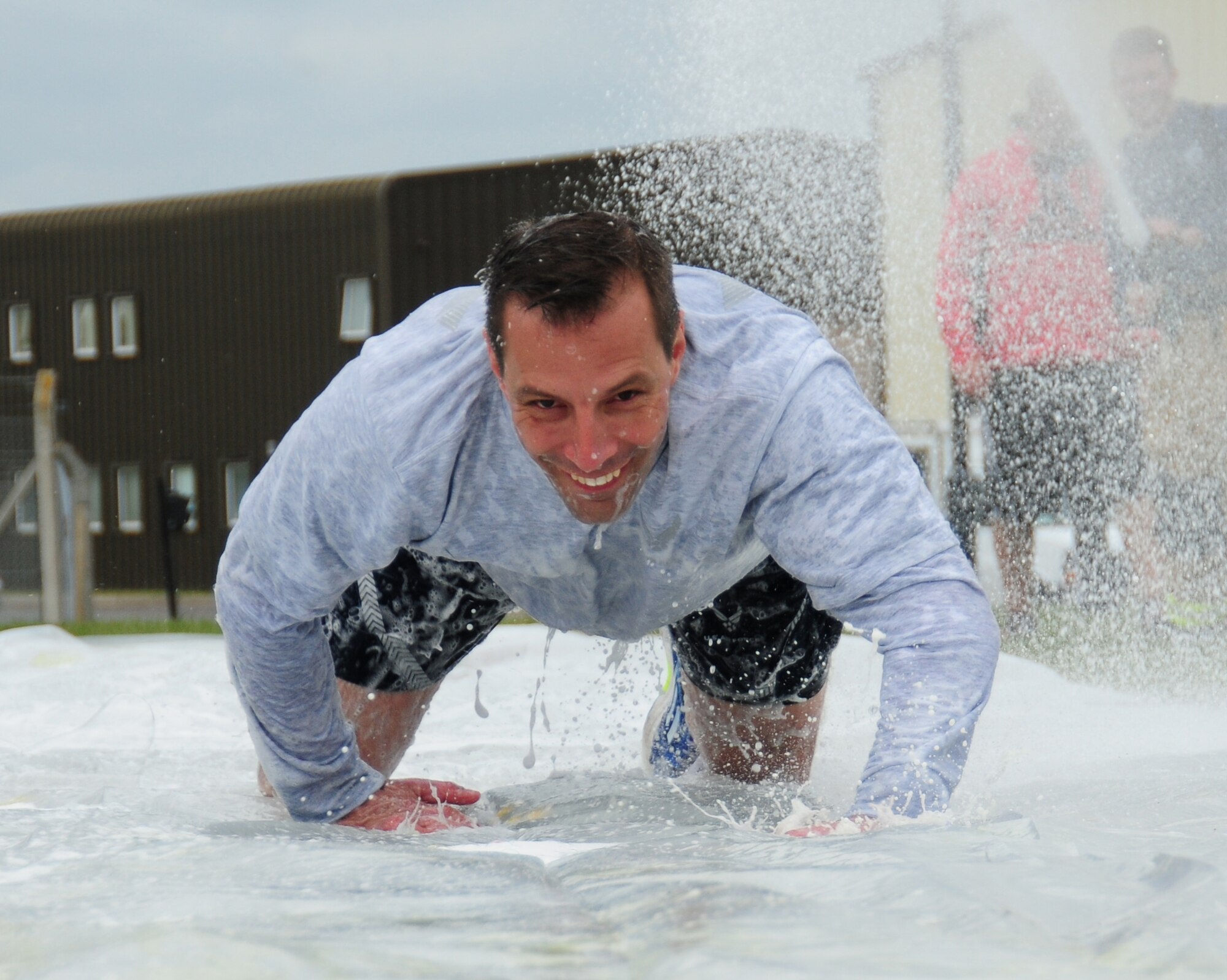 Col. Christopher Kulas, 100th Air Refueling Wing commander, low-crawls along a “slip-n-slide’” at a post Unit Effectiveness Inspection celebration sports challenge May 10, 2013, at RAF Mildenhall, England. After a Team Mildenhall formation run around the taxiway and perimeter road, Airmen participated in events including tug of war, arm wrestling and hurdles. (U.S. Air Force photo by Karen Abeyasekere/Released)