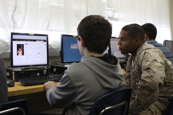 Cpl. Ronald Watts Jr., a station Provost Marshal’s Office special reaction team member and “Adopt-a-School” program volunteer, helps a Matthew C. Perry student look up material for a research paper at the M.C. Perry High School opportunity hall here May 13, 2013. The “Adopt-a-School” program came about as a way to monitor and help at-risk students. Students must have two Fs or a 2.00 grade point average or less to qualify.