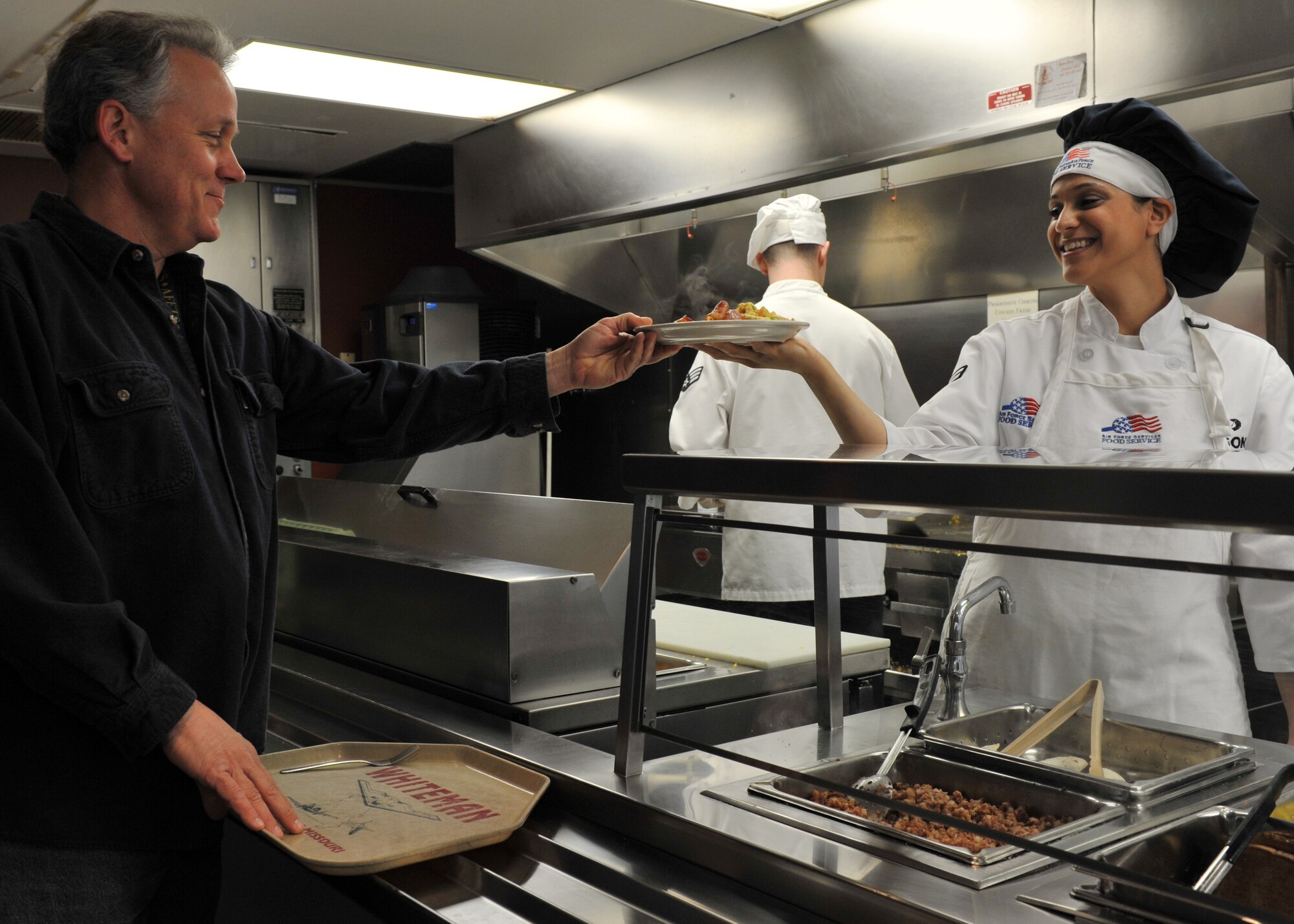 Airman 1st Class Taqla (Tina) Eidson, Force Support Squadron food service specialist, hands a customer breakfast during the Hennessy Evaluation at the Touch N’ Go In-Flight Kitchen at Whiteman Air Force Base, Mo., April 3, 2013. Winners must display excellence in management effectiveness, force-readiness support, food quality, employee and customer relations, resource conservation, and training and safety awareness. (U.S. Air Force photo by Heidi Hunt/Released)