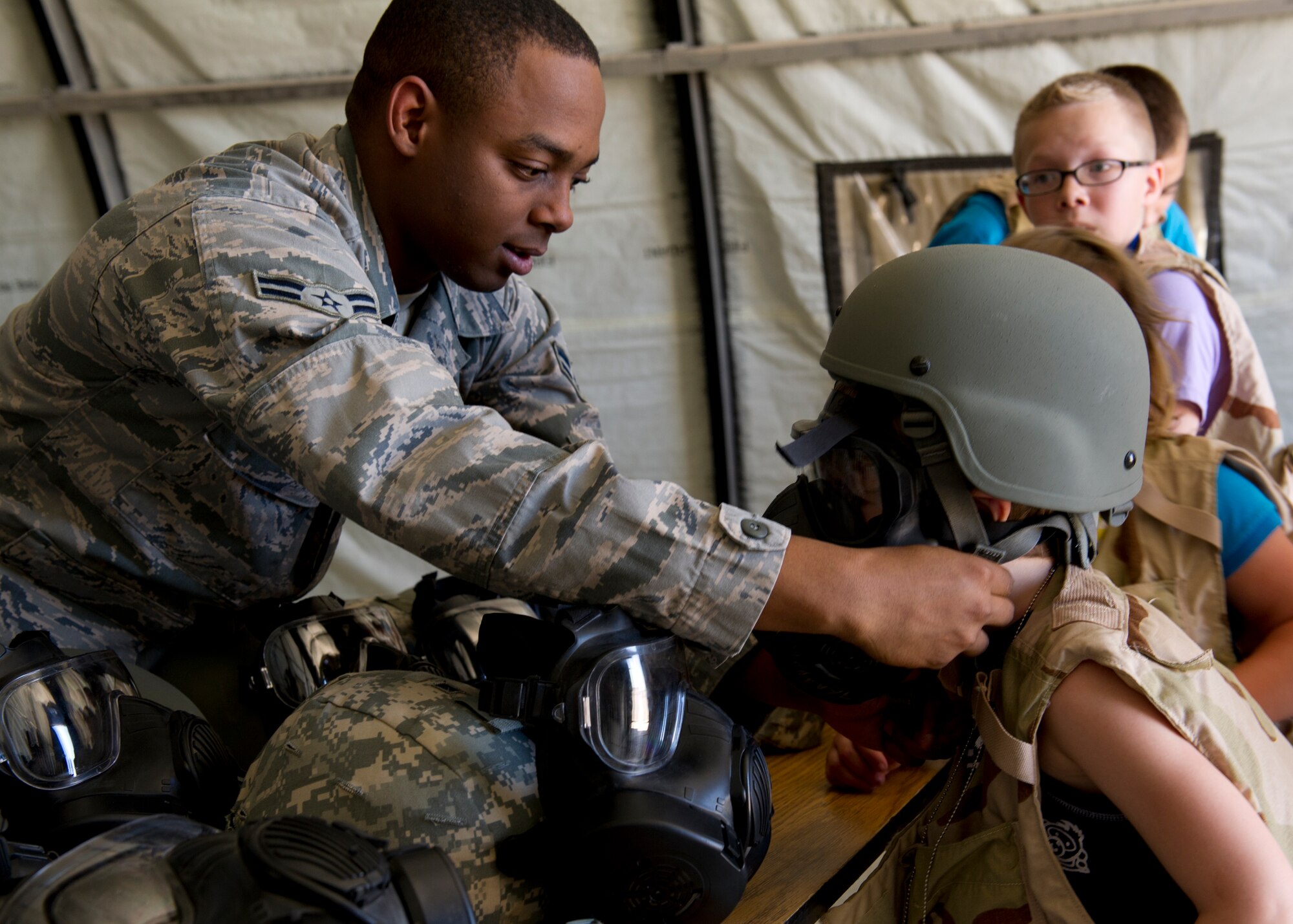 Airman 1st Class Trevin Nesbitt, 49th Logistics Readiness Squadron logistics planning technician, assists a “deployer” with putting on a helmet at “Bearghanistan” during Operation Kids Investigating Deployment at Holloman Air Force Base, N.M., May 13. Operation K.I.D. gave the “deployers” an inside look at what their parents go through when called to deploy. (U.S. Air Force photo by Senior Airman Kasey Close/Released)