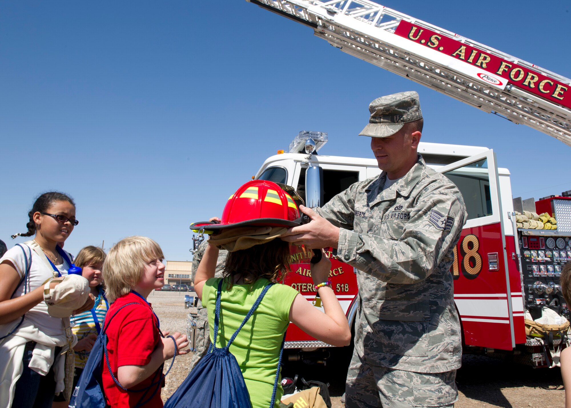 Staff Sgt. Bobby Roberts, 49th Civil Engineer Squadron firefighter, assists a child with putting on a firefighter’s helmet at deployment to “Bearghanistan” during Operation Kids Investigating Deployment at Holloman Air Force Base, N.M., May 13. The “deployers” experienced a recall, deployment line, deployment to “Bearghanistan,” and welcome home. (U.S. Air Force photo by Senior Airman Kasey Close/Released)