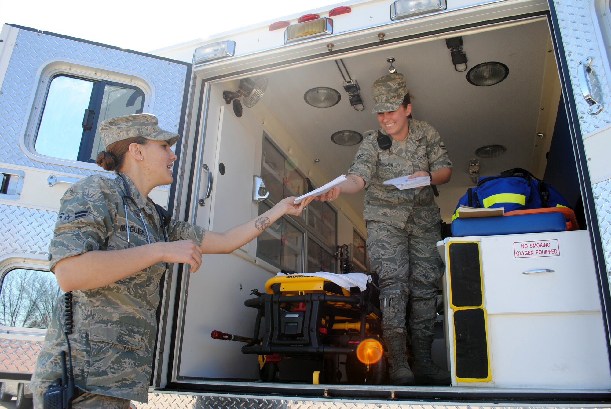 (Right) Airman 1st Class Alexys Ramkishun, 319th Medical Operation Squadron emergency medical technician, hands information pamphlets to her fellow paramedic, Airman 1st Class Alexandria McGuire, outside an ambulance used as a static display May 7, 2013, on Grand Forks Air Force Base, N.D. The static display was one of the items featured during the second of five days designated for this year’s Nurse-Tech Week. (U.S. Air Force photo/Staff Sgt. Luis Loza Gutierrez)
