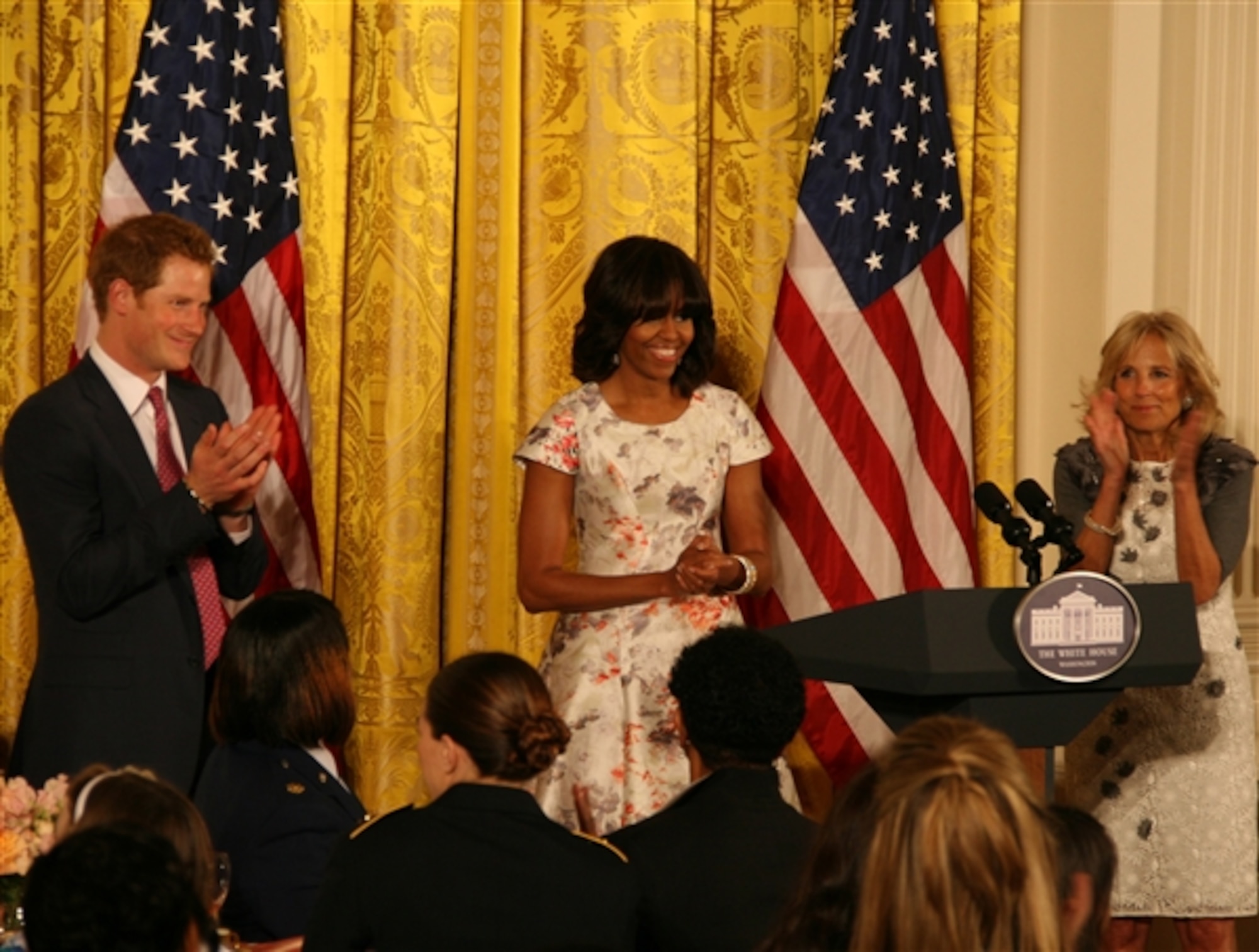 First lady Michelle Obama, center, Dr. Jill Biden, right, and Britain’s Prince Harry applaud military families, May 9, 2013, in the East Room of the White House at the Joining Forces Mother’s Day Tea. (Department of Defense photo by Terri Moon Cronk/Released)