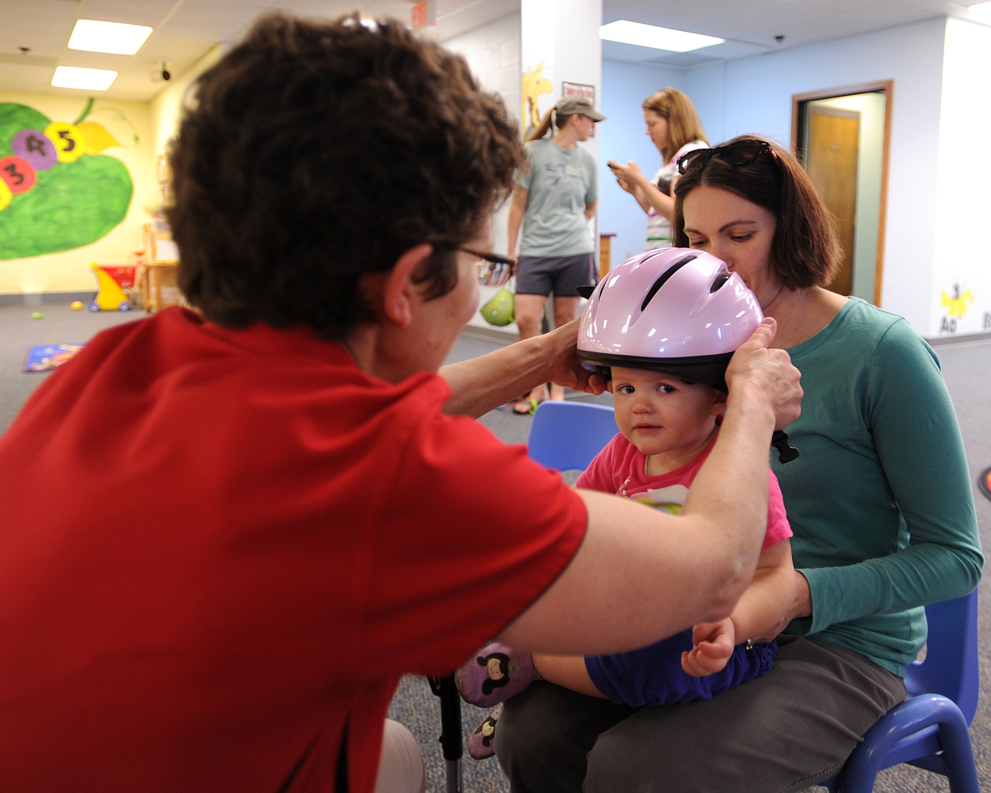 Patty Olsen, Safe Kids Grand Forks sports coordinator, fits a toddler helmet on 15-month-old Mia Kropf on May 14, 2013, on Grand Forks Air Force Base, N.D.  Personnel from Safe Kids Grand Forks visited the base to help teach parents and youth how to properly wear bike helmets. (U.S. Air Force Photo/ Airman 1st Class Xavier Navarro) 