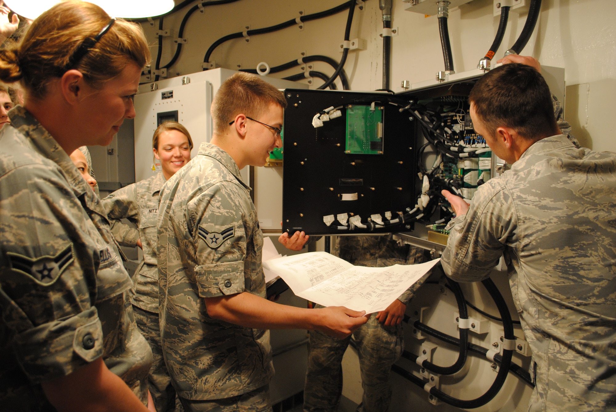 Airman 1st Class Tripp McCool, 341st Missile Maintenance Squadron technician, looks over a Technical Order schematic while Staff Sgt. Josh Young, 341st MMXS Electromechanical Team instructor, points out major components on the Secondary Door Control Assembly at the T-41 trainer to his students.  Airman 1st Class Danielle Ellis, 341st Maintenance Group member (left), and other students look on.  (U.S. Air Force photo/Senior Airman Cortney Paxton)