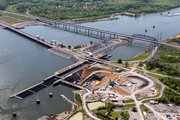 This aerial photo of the Kentucky Lock Addition project taken April 26, 2013 in Grand Rivers, Ky., shows construction of a new 1200-foot lock landward of the existing 600-foot lock and the relocated highway and railroad bridges downstream of the dam. The upstream-bound split barge tow will be able to lock through as a single tow when the new lock is completed by the U.S. Army Corps of Engineers Nashville District in partnership with the Tennessee Valley Authority. (USACE Photo)