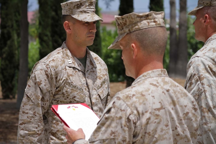 Captain Ryan D. Schramel, the former commanding officer of Weapons Company, 2nd Battalion, 4th Marine Regiment, stands in front of a formation of Marines as Sgt. Maj. Gary T. Bow, the battalion sergeant major, reads Schramel's award citation for the Bronze Star Medal with Combat "V" for valor during a ceremony at the 5th Marines Memorial Garden here, May 16, 2013. Schramel, a native of Taylorsville, Calif., was awarded the Bronze Star for leading his company of Marines through multiple combat operations and engagements with insurgents in the Now Zad district of Helmand province, Afghanistan. During an operation dubbed Western Gambit, Schramel was directly responsible for the tactical employment of more than 350 Marines and Afghan soldiers and police through an insurgent infested area of the Now Zad district, resulting in the control of the area. The operation was planned as a helicopter-borne assault, but foul weather cancelled all air support and the Marines resorted to ground movements exposing themselves to the unfamiliar terrain in the insurgent infested area. As the weather worsened with rain and the terrain accumulated mud and flooding, Schramel and his Marines pushed on. They reached the village of Khurghay where they were met with heavy resistance from the enemy. Insurgents manned multiple heavy machine gun positions that briefly suppressed the Marines' mission. Undeterred from the weather elements and the enemy, Schramel rallied his Marines and maneuvered two of his platoons south of the village, encircling the enemy. He then directed a counterattack that crushed the entire enemy resistance in the area and controlled the village. The actions of the Marines and Afghan security forces resulted in the eventual establishment of an Afghan Uniformed Police post in Khurghay.