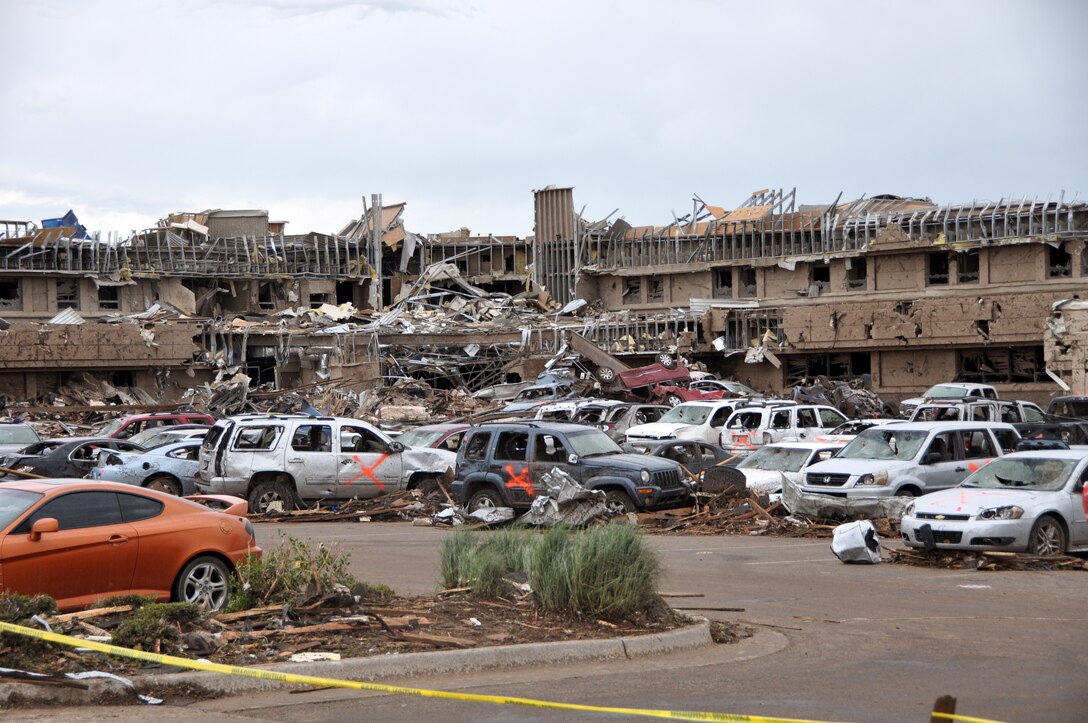 The Moore Medical Center – Norman Regional Hospital in Moore Okla., is ripped apart by the massive tornado on May 20, 2013.  The hospital was directly in the path of the 1.3 mile wide tornado that hit Moore in the late afternoon.  There were no casualties reported.  Cars flipped over and piled on top of one another along with cars that were cleared away by first responders fill the parking lot.  The Orange X spray painted on the cars indicates that the vehicle was checked and cleared of any victims.  (U.S. Air Force photo by Senior Airman Mark Hybers)
