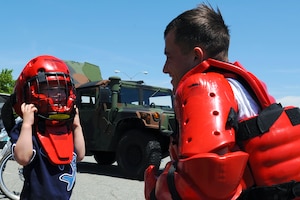 Staff Sgt. Kelly Eaton, 633rd Security Forces Squadron Krav Maga instructor, watches as 4-year-old Mason Gilbert, son of Maj. Myles Gilbert, Air Combat Command program manager, tries on a security forces helmet during Police Week at Langley Air Force Base, Va., May 15, 2013. One of Police Week’s events was a demonstration day, held in the Exchange parking lot for the community. (U.S. Air Force photo by Airman 1st Class Victoria H. Taylor/Released)