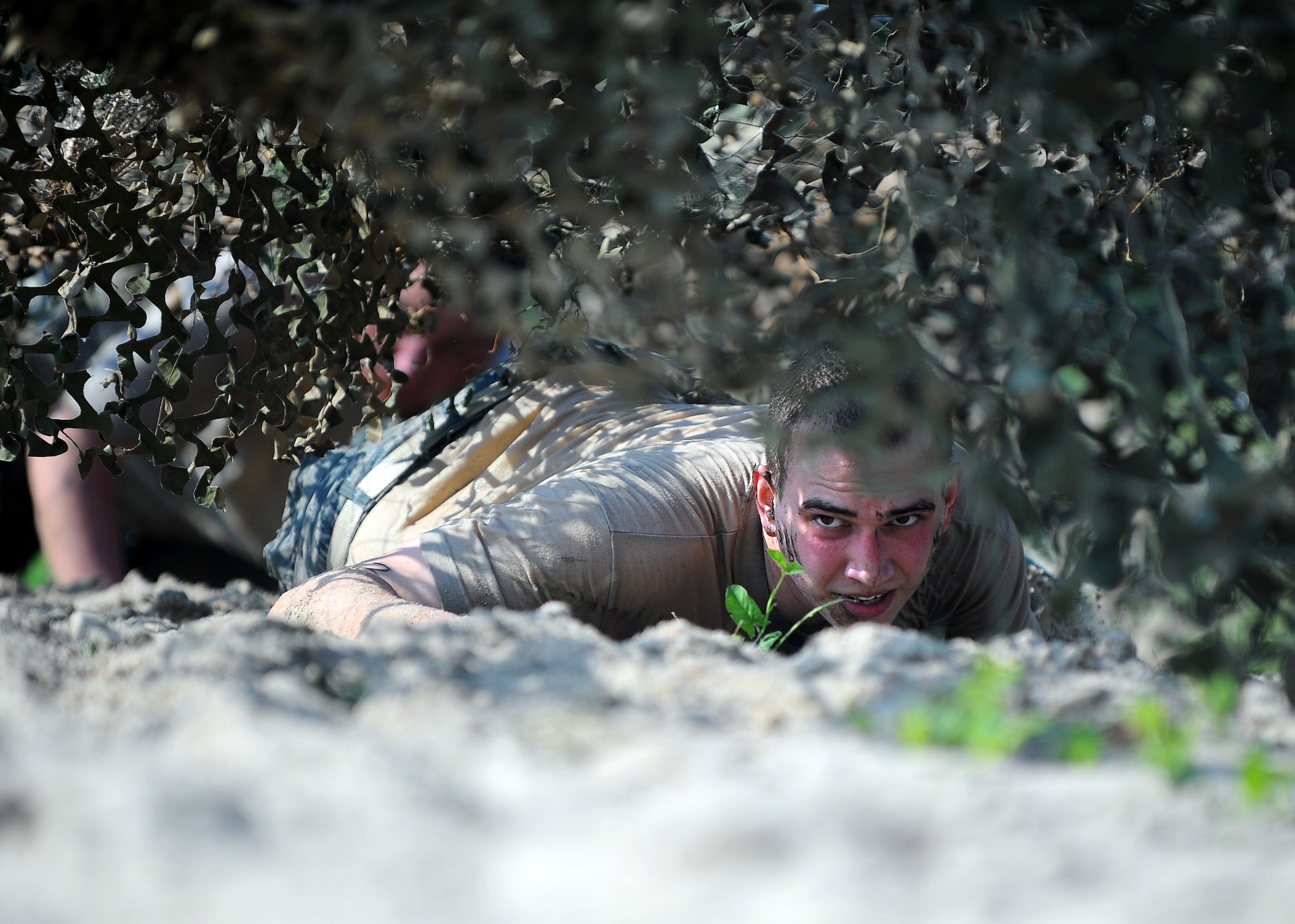 U.S. Air Force Staff Sgt Jordan Hoyt, fuels service center controller with the 55th Logistics Readiness Squadron Petroleum, Oils and Lubricants Flight, does a low crawl under a camouflage canopy while competing in the Police Week Evasion Challenge obstacle course held on May 16, Offutt Air Force Base, Neb. The Evasion Challenge tested participants both physically and mentally. (U.S. Air Force photo by Josh Plueger/Released)