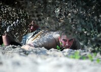 U.S. Air Force Staff Sgt Jordan Hoyt, fuels service center controller with the 55th Logistics Readiness Squadron Petroleum, Oils and Lubricants Flight, does a low crawl under a camouflage canopy while competing in the Police Week Evasion Challenge obstacle course held on May 16, Offutt Air Force Base, Neb. The Evasion Challenge tested participants both physically and mentally. (U.S. Air Force photo by Josh Plueger/Released)