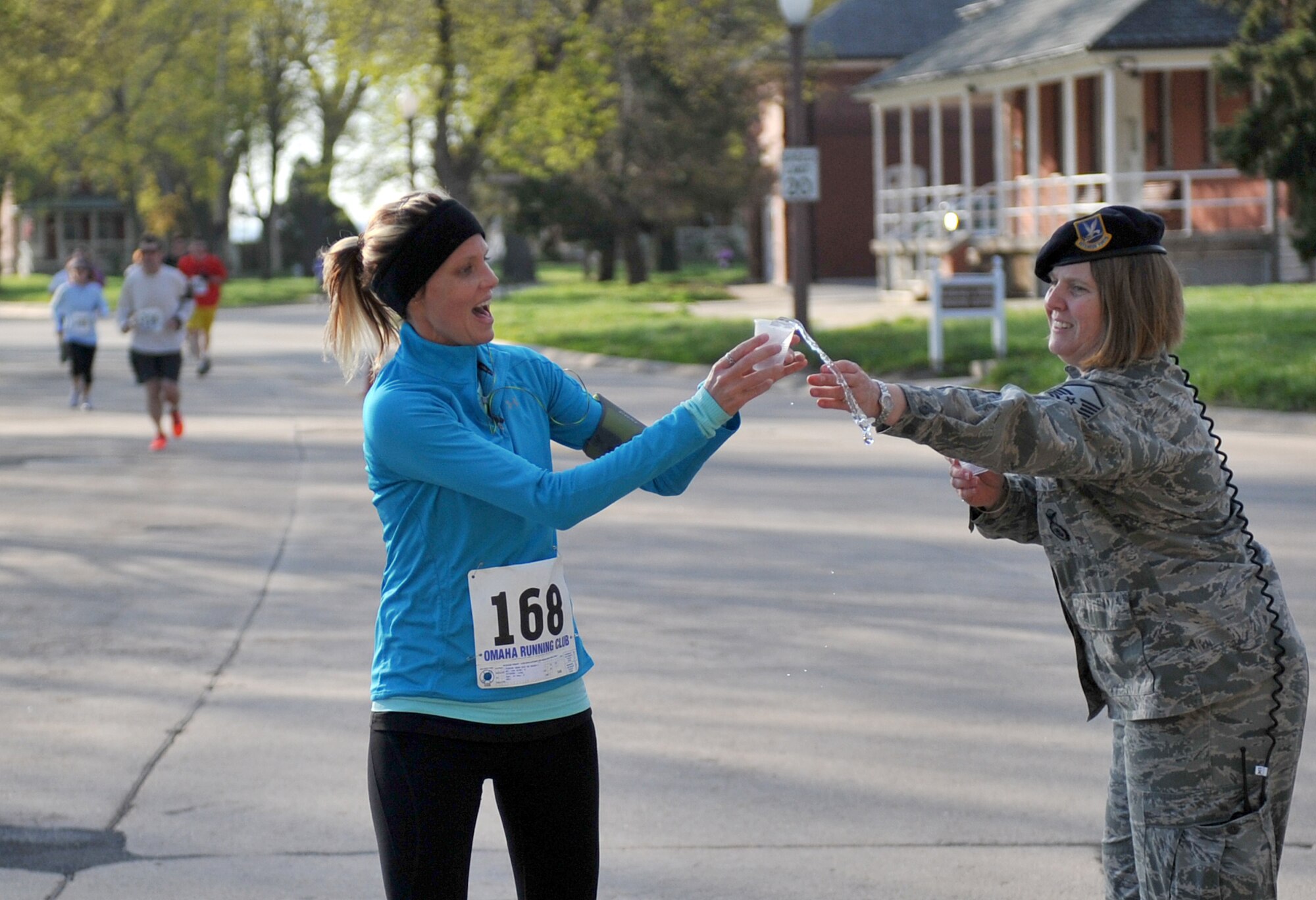 Sarah Stahl tries to grab a cup of water from Master Sgt. Theresa Sutton from the 55th Security Forces Squadron at the five-mile water check point located by Generals’ Row. More than 200 patrons were participated in the annual Bellevue-Offutt Runway Run at Offutt Air Force Base, Neb., May 12. The annual Mother's Day run is a unique, seven mile race that takes runners past parked aircraft and through the historic parade grounds and housing area. (U.S. Air Force photo by Jeff W. Gates/Released)