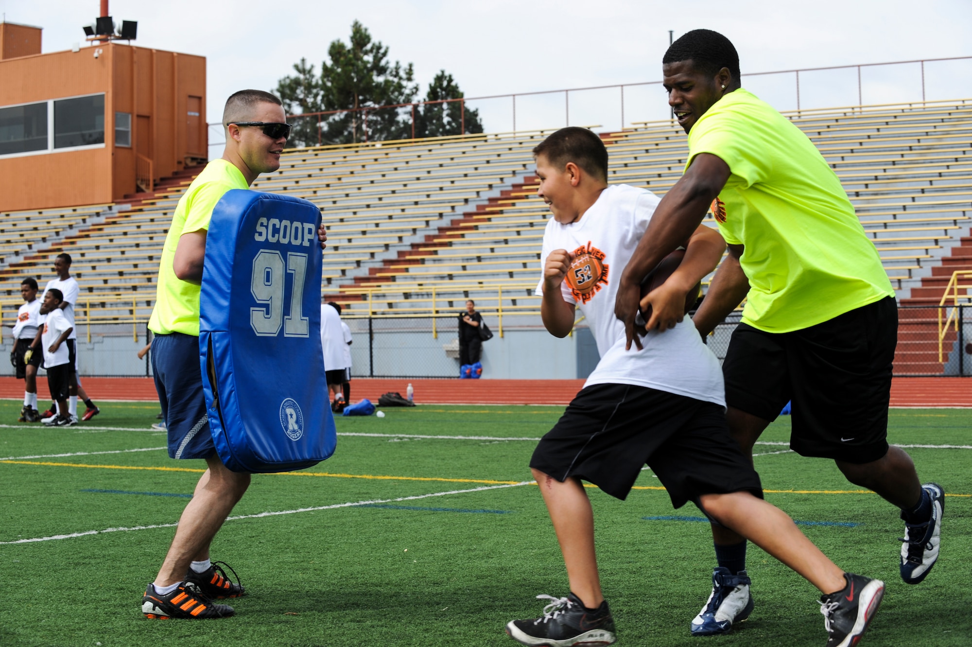 Timothy Barnhart, left, anticipates a hit from a 16Ways football camp participant as Maurice Greer, right, attempts to fumble the ball May 18, 2013, at the Aurora Public Stadium, Aurora, Colo. Barnhart, an Air Force staff sergeant with the 460th Medical Group, was one of about 30 volunteers from Buckley Air Force Base to participate in the camp, which focused on basic football fundamentals, teamwork and anti-bullying. (U.S. Air Force photo by Staff Sgt. Christopher Gross/Released)